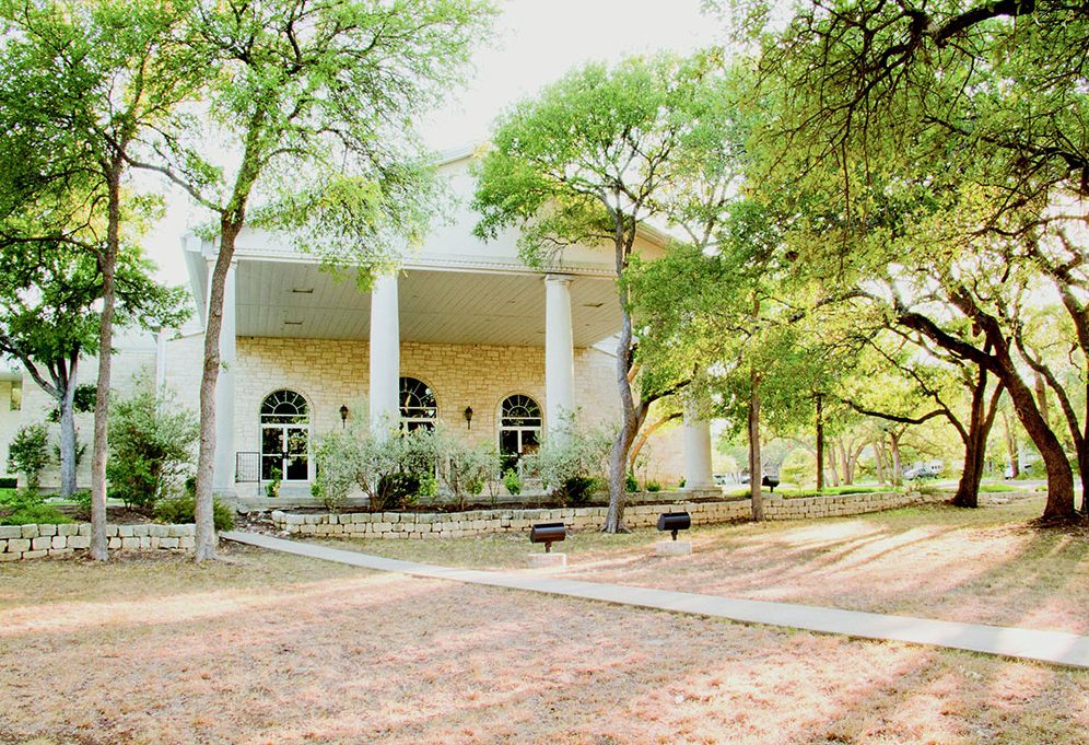 Covered entrance with white columns at Austin International School, surrounded by oak trees