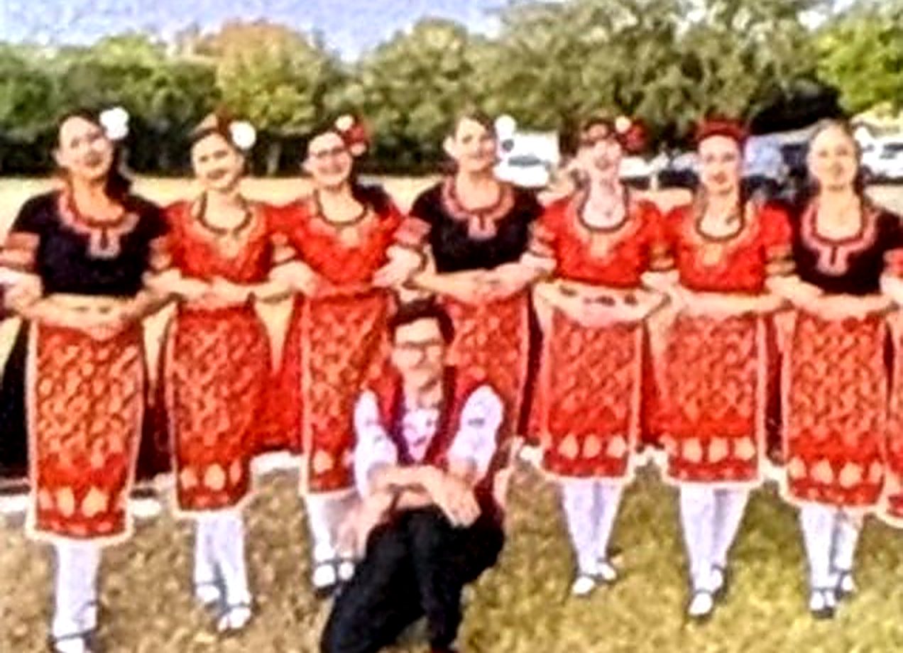 Zdravets dancers in red costumes lined up on the grass